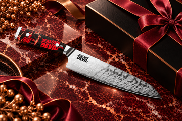 Jealous Devil chef knife on burgundy marble with copper accents.