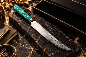 Chef Supply Co kitchen knife with an iridescent blue-green handle and patterned blade on black marble with gold accents.