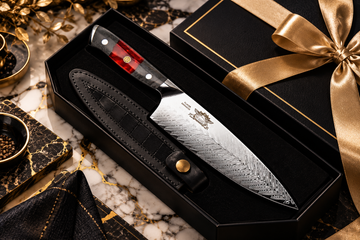 Kitchen knife with a patterned steel blade in a black gift box with a gold ribbon on a black and gold marble surface.