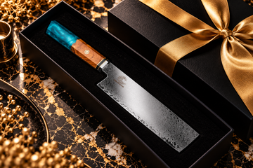 Luxury chef’s cleaver with a teal and wood handle in a black gift box on black marble with gold ribbon.