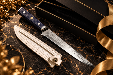 Kitchen knife with a navy honeycomb handle and patterned blade beside a cream sheath on black marble with gold accents.