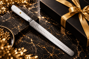 Luxury chef’s cleaver with a teal and wood handle in a black gift box on black marble with gold ribbon.