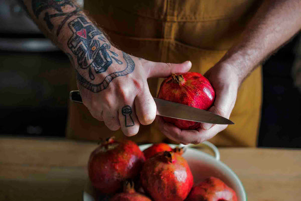 Chef with paring knife prepares pomegranates. 